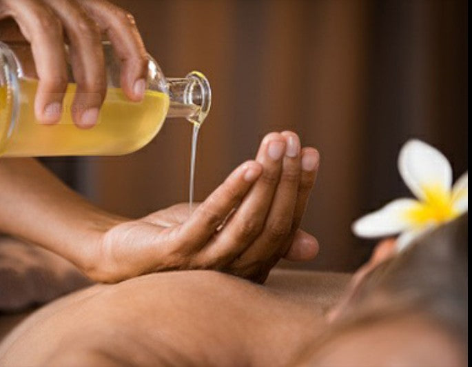 woman pouring massage oils into her hand whilst touching a mans back with an out of focus flower in the background
