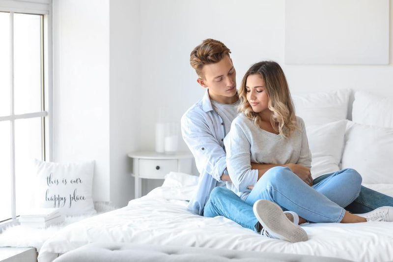 Couple relaxing on a bed with soft pastel beginner-friendly intimacy products from the Perfect Embrace collection.